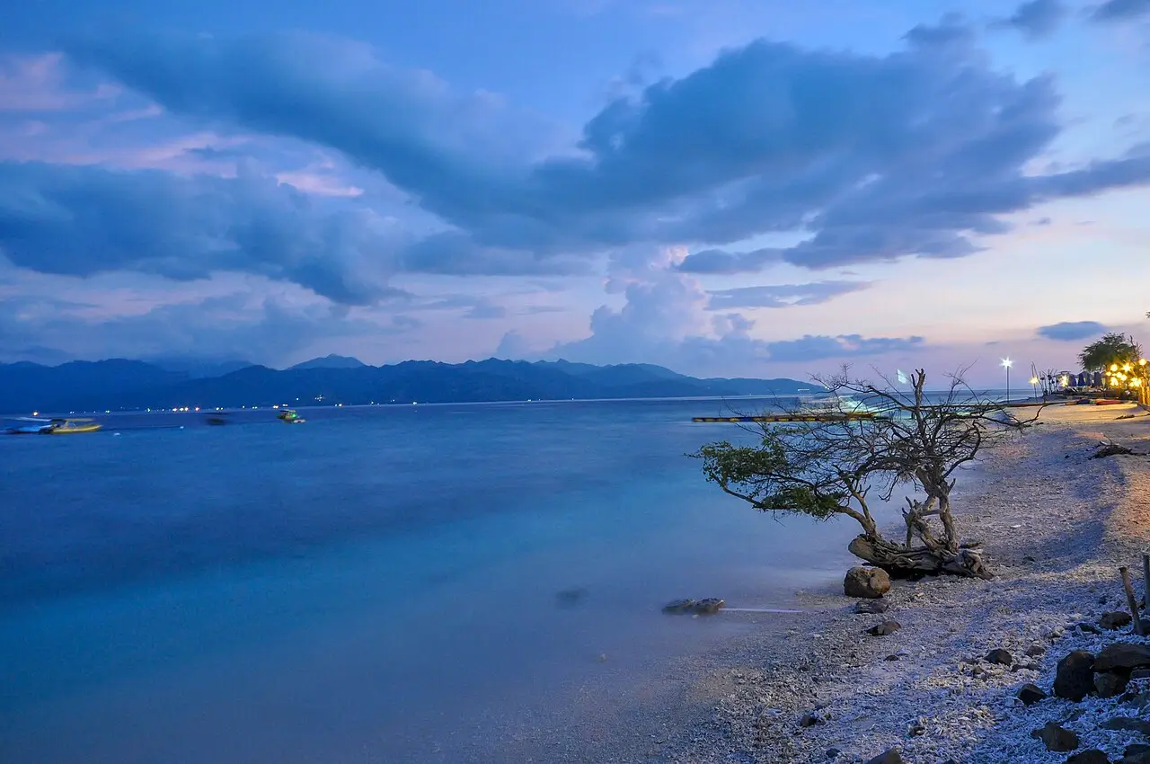 Peaceful shoreline and calm ocean at dusk in Gili Trawangan with mountains visible across the water.