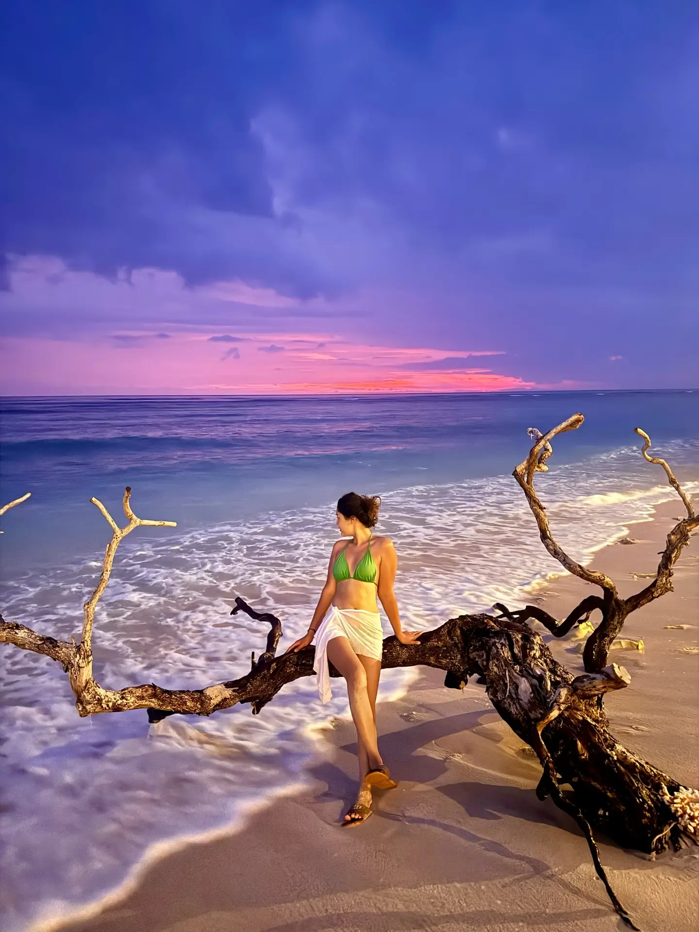 Visitor relaxing on driftwood along a quiet beach at sunset in Gili Trawangan.